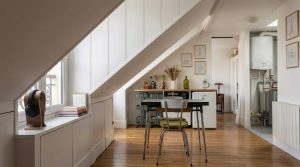 Bright attic conversion featuring sloped white walls, built-in storage, and a compact wooden dining table on hardwood floors.