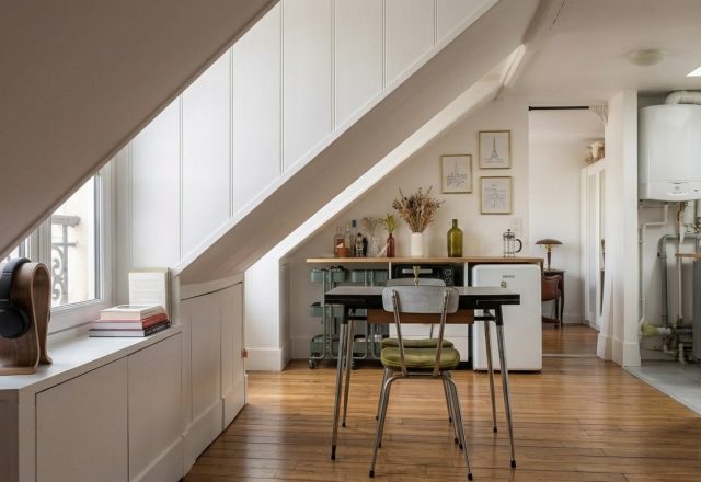 Bright attic conversion featuring sloped white walls, built-in storage, and a compact wooden dining table on hardwood floors.