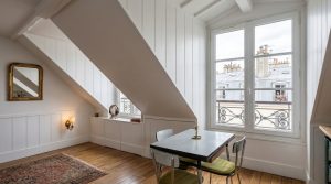 Bright attic dining room featuring a small table, sloped white walls, and a large dormer window.