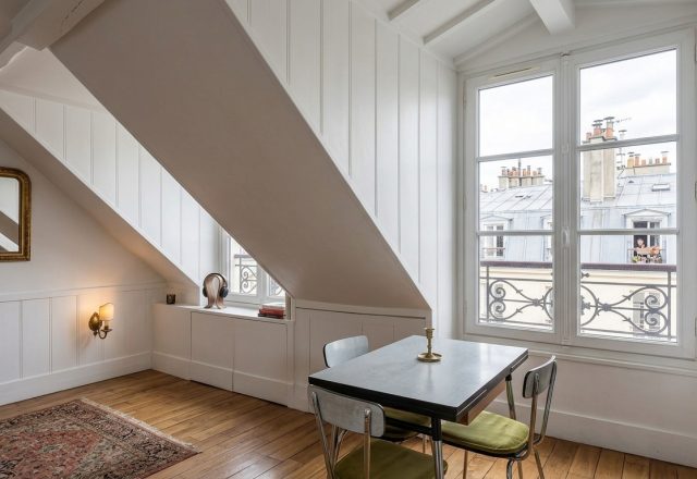 Bright attic dining room featuring a small table, sloped white walls, and a large dormer window.