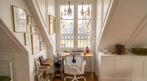 Bright attic home office setup featuring a wooden desk under a sloped window and a gallery wall.