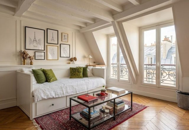 Bright attic living room design featuring white daybed, herringbone floors, and sloped ceiling beams.