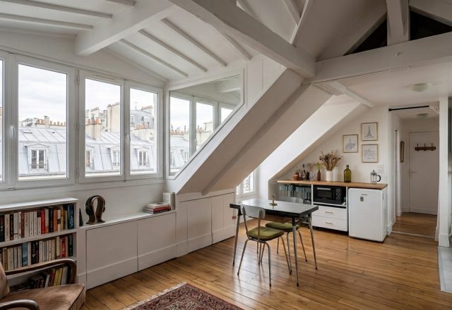 Bright attic living room design featuring sloped ceilings, white exposed beams, and custom built-in bookshelves.