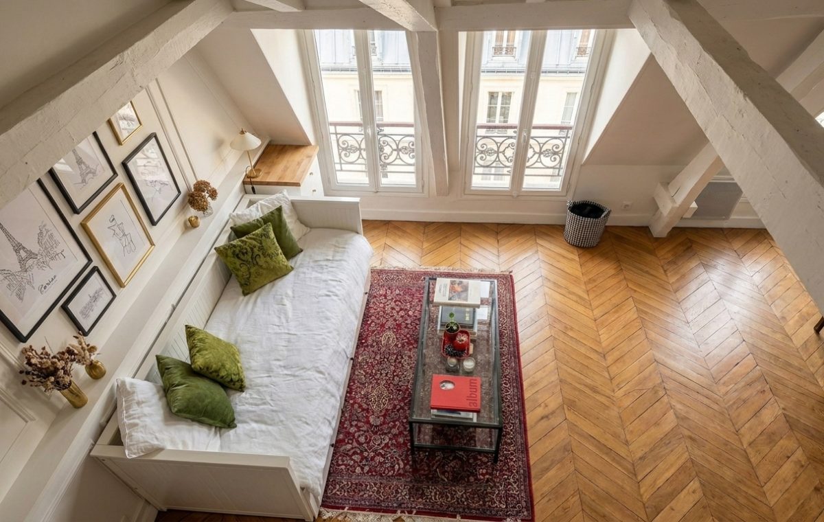 Bright attic living room with sloped ceilings, a white daybed, chevron wood floors, and twin dormer windows.