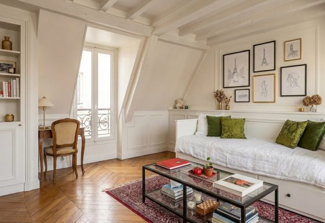 Bright attic living room with sloped ceilings, built-in shelving, white daybed, and chevron wood floors.
