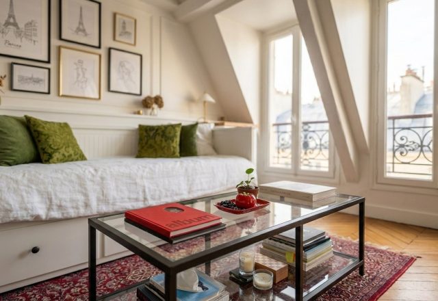 Cozy attic living room featuring a white daybed, glass coffee table, and slanted ceilings under tall windows.