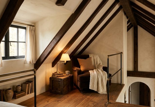 Cozy attic loft conversion featuring exposed wooden beams, sloped ceilings, and a built-in reading nook with a velvet armchair.