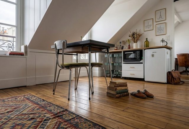 Cozy attic studio apartment interior featuring sloped ceilings, hardwood floors, compact dining area, and mini-fridge setup.