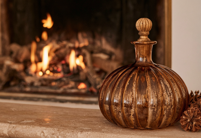 Amber glass bottle and pinecones styled on a stone fireplace mantel during autumn.