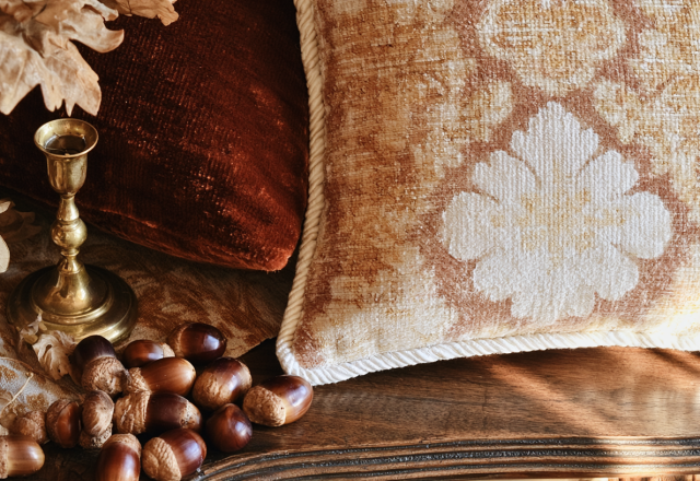 Close-up of autumn home decor featuring velvet pillows, brass candlestick, and acorns on a wooden surface.