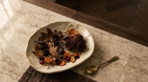 Speckled ceramic dish filled with dried autumn leaves and roses on a marble countertop for autumn home decor styling.