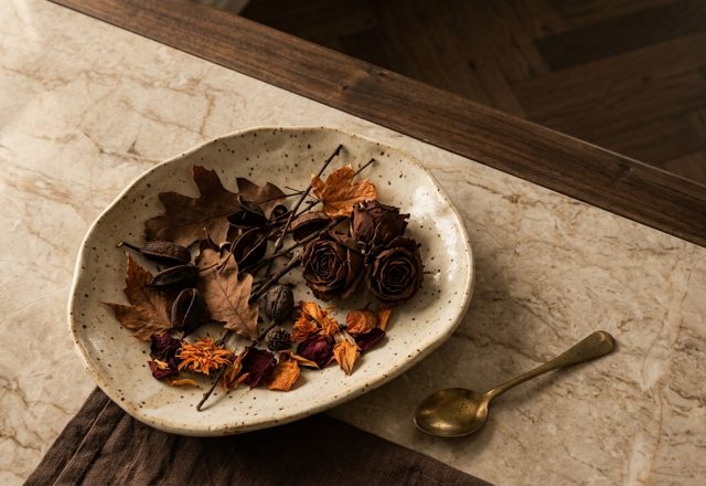 Speckled ceramic dish filled with dried autumn leaves and roses on a marble countertop for autumn home decor styling.