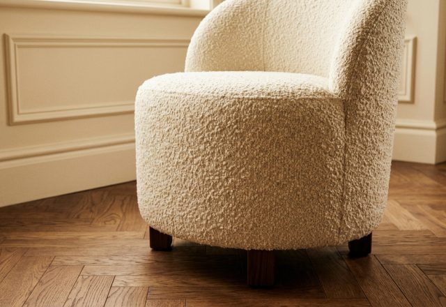 A cozy cream boucle accent chair with dark wooden legs sitting on a herringbone parquet floor.