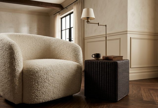 A cozy cream boucle swivel chair next to a dark woven side table and brass lamp in a neutral living room.