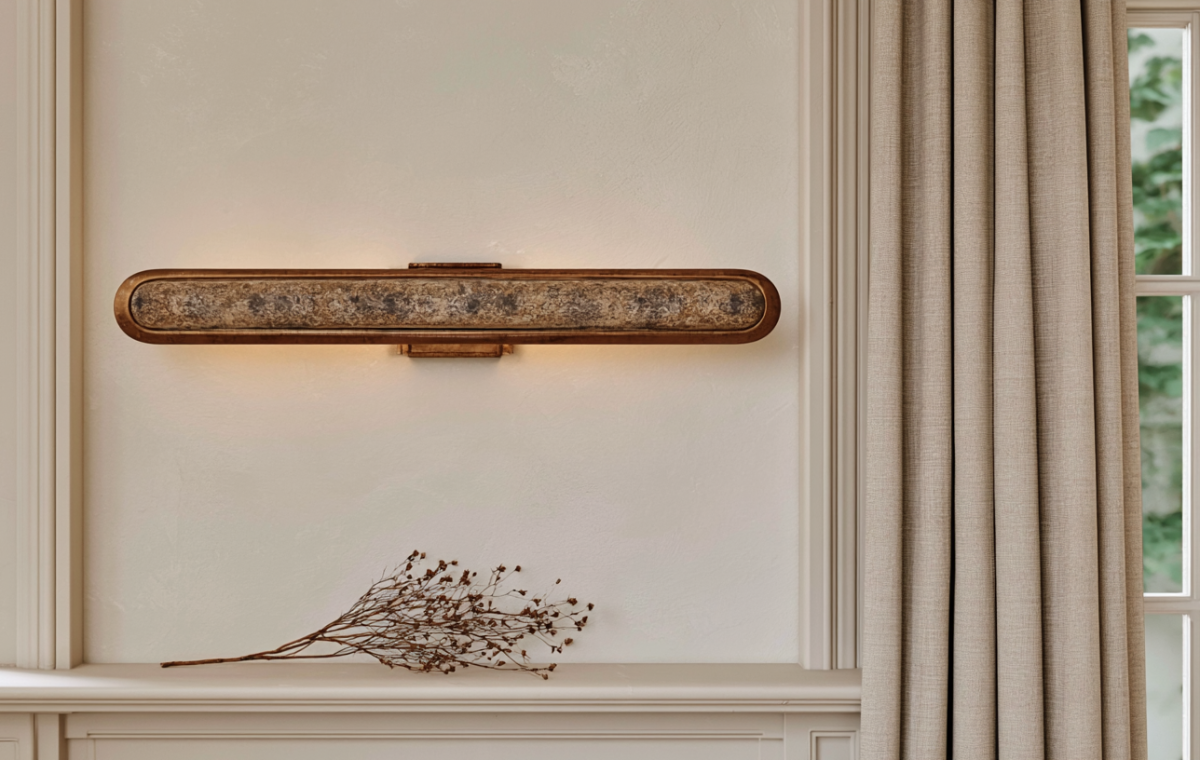 Elongated brass wall sconce casting warm ambient light on a neutral living room wall