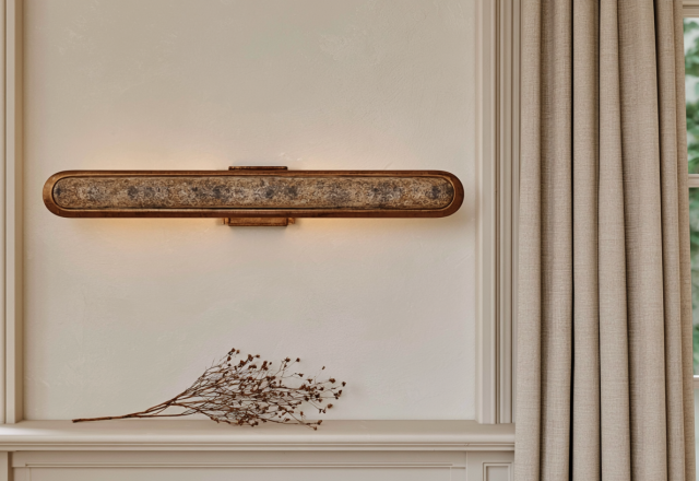 Elongated brass wall sconce casting warm ambient light on a neutral living room wall