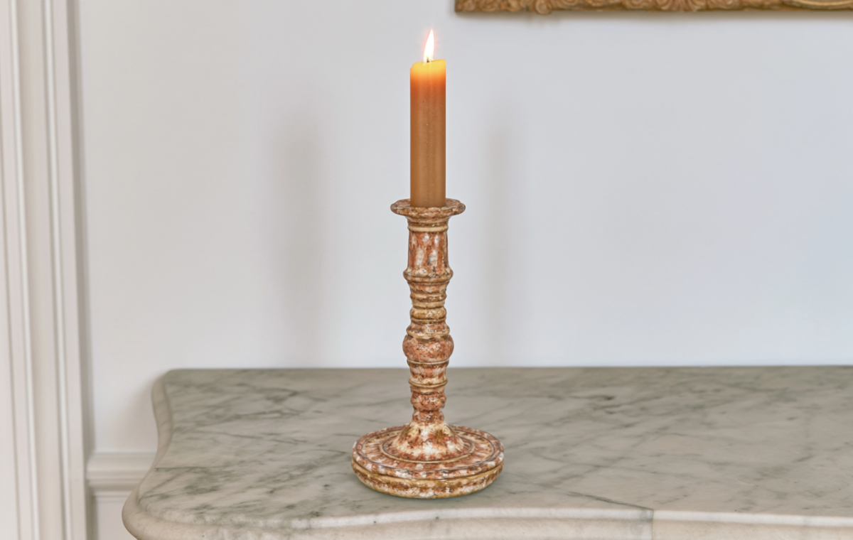 A handcrafted ceramic candle holder with a burning taper resting on a marble console table.