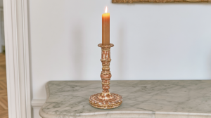 A handcrafted ceramic candle holder with a burning taper resting on a marble console table.