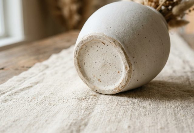 Close-up of a rustic ceramic vase base resting on a textured neutral table runner.