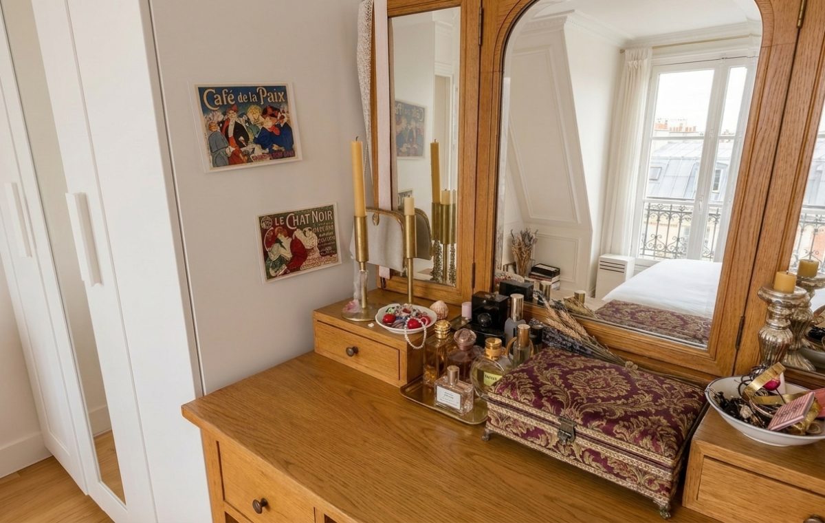 A warm wooden vanity setup featuring a triple mirror, vintage art prints, and organized perfume bottles.