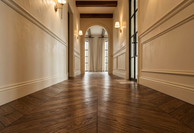 Rich brown chevron hardwood flooring in a bright transitional hallway with wainscoting and brass sconces.
