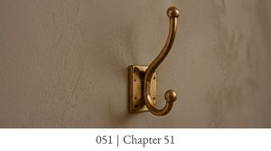 A sturdy brass wall hook mounted on textured plaster with visible screw fixings.