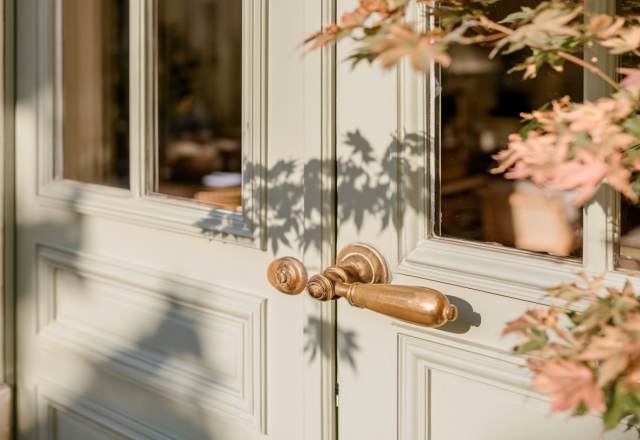 Close up of pale green front entryway double doors with polished brass hardware and morning sunlight shadows