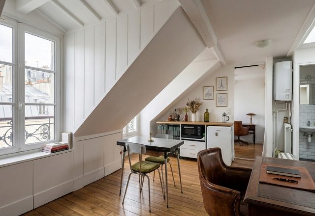 Bright attic home office layout featuring slanted white ceilings, wooden floors, and a leather desk chair.