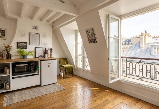 Bright attic kitchen featuring sloped ceilings, wooden countertops, and a view of Parisian rooftops through casement windows.