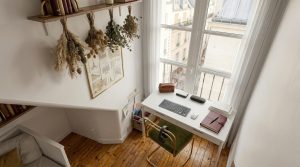 Bright small home office setup featuring a white desk, green velvet chair, and tall window.