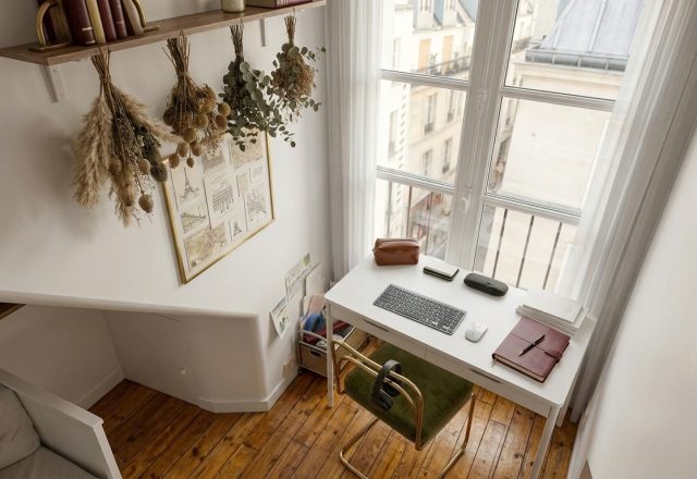 Bright small home office setup featuring a white desk, green velvet chair, and tall window.