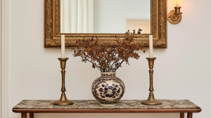 Console table styling featuring an antique gold mirror, vintage brass candlesticks, and a blue and white ceramic vase.