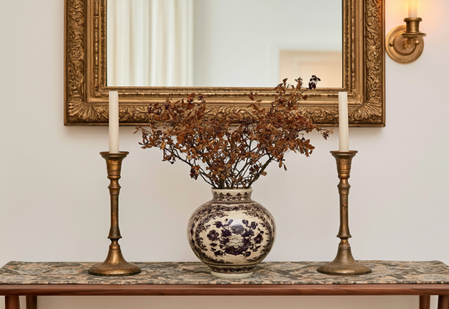 Console table styling featuring an antique gold mirror, vintage brass candlesticks, and a blue and white ceramic vase.