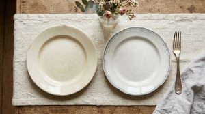A rustic table setting featuring mismatched ceramic plates, a textured runner, and a vintage silver fork on a wooden table.