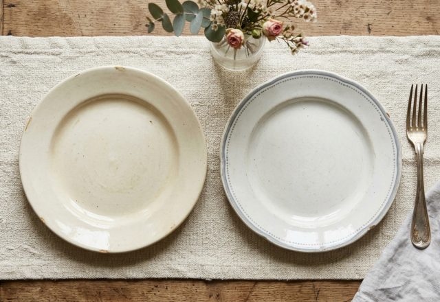A rustic table setting featuring mismatched ceramic plates, a textured runner, and a vintage silver fork on a wooden table.
