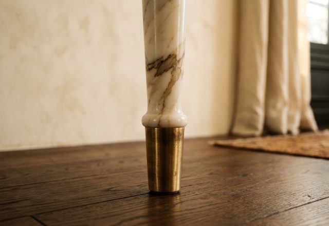 Close-up of luxury marble table legs with a brass metal ferrule resting on dark hardwood floors.