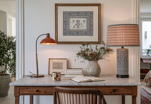 A cozy home office desk setup featuring a marble top wooden desk, vintage lamps, and framed art.