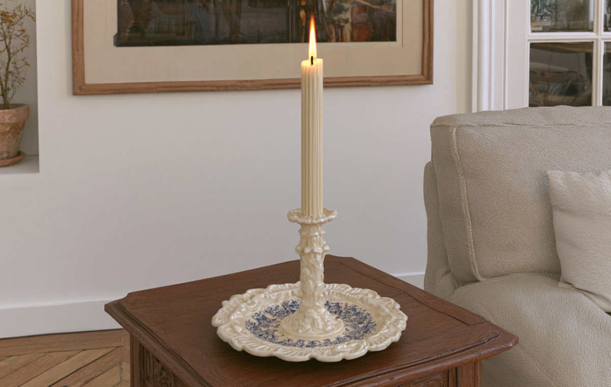 A ribbed pillar candle in a decorative ceramic holder rests on a dark wooden side table in a cozy living room.