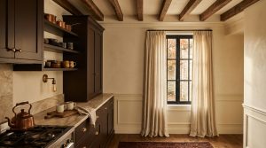 Dark kitchen cabinets paired with exposed wooden beams, marble countertops, and neutral linen curtains.