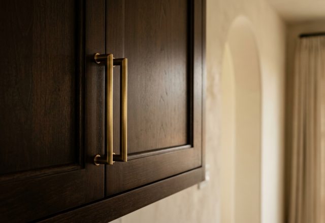 Close up of dark wood cabinets featuring sleek brushed brass hardware pulls in a transitional interior space.