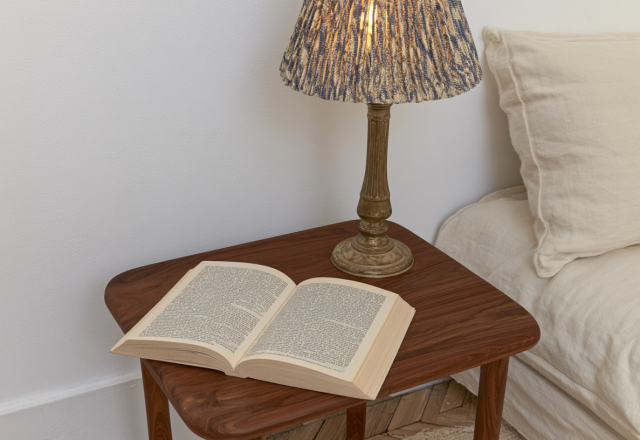 A cozy bedside reading nook featuring a walnut nightstand, open book, and a textured lamp next to a neutral bed.