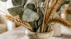 Dried eucalyptus and wheat decor arranged inside a rustic speckled ceramic vase on a wooden tabletop.