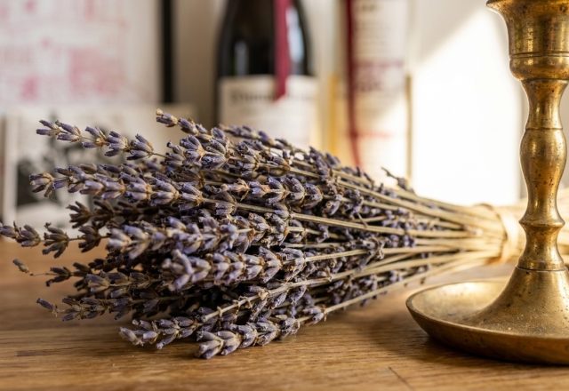 Dried lavender decor bundle lying next to a vintage brass candlestick on a wooden tabletop.