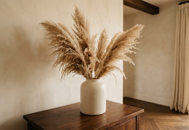 Dried pampas grass decor in a matte ceramic vase on a wooden console table against a textured beige wall.