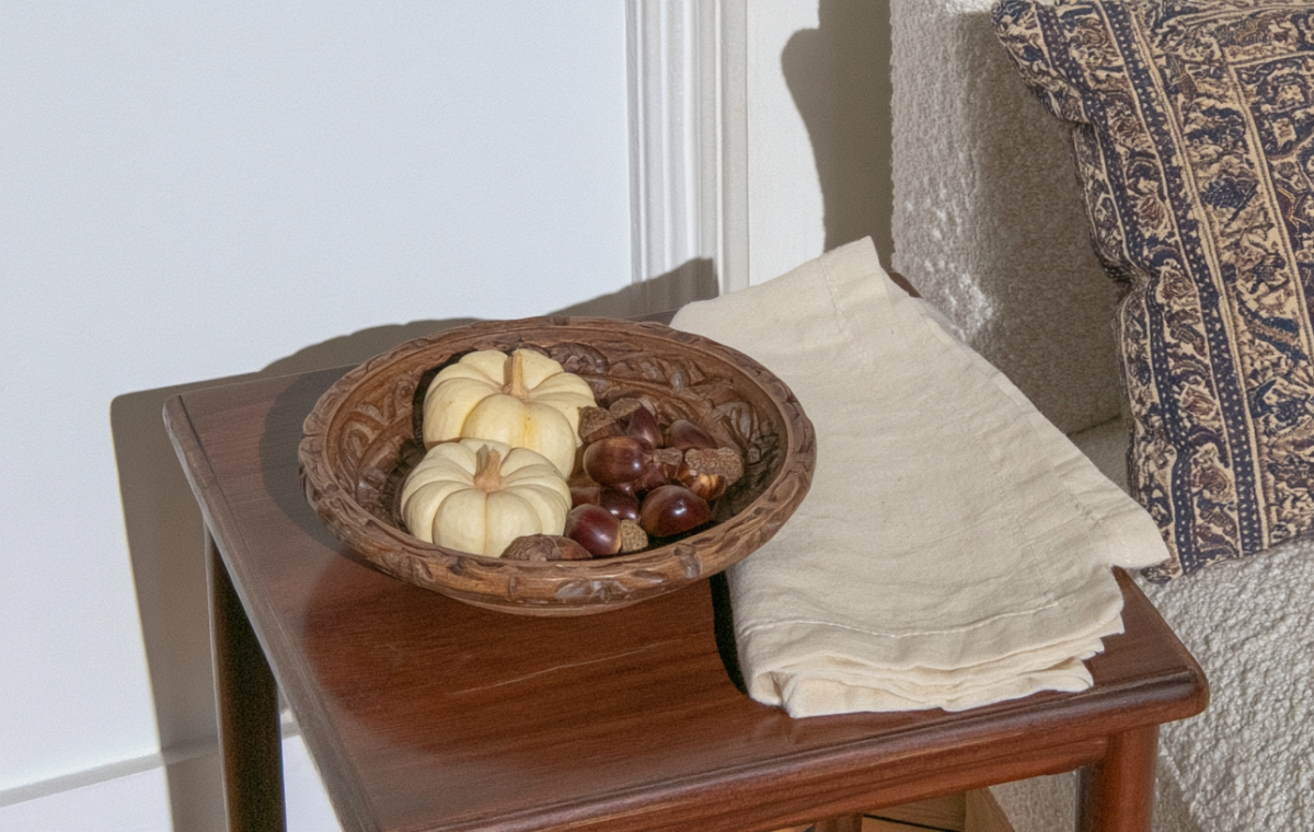 Autumn side table decor featuring a wooden bowl with mini pumpkins and chestnuts next to a cream sofa.