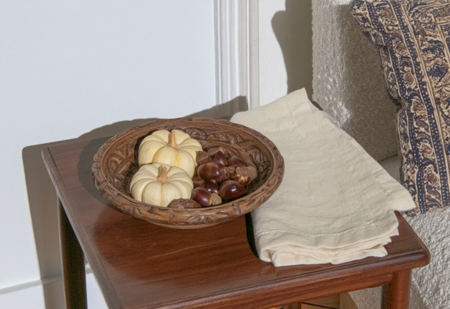 Autumn side table decor featuring a wooden bowl with mini pumpkins and chestnuts next to a cream sofa.