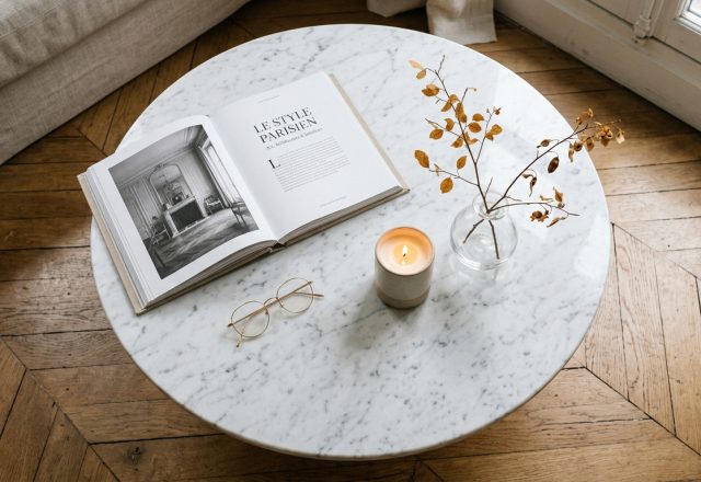 Minimalist coffee table styling with an open art book, wire glasses, candle, and dried branches on a marble top.