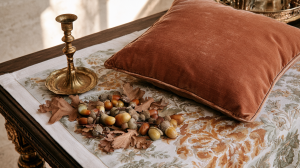 Fall home decor featuring a velvet pillow, brass candlestick, and acorns on a wooden table.