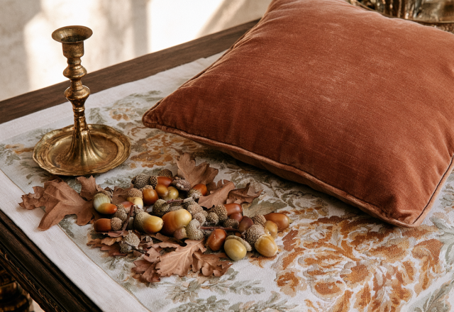 Fall home decor featuring a velvet pillow, brass candlestick, and acorns on a wooden table.