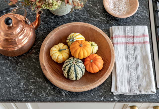 Kitchen autumn decor featuring mini pumpkins in a wooden bowl next to a copper kettle on a marble countertop